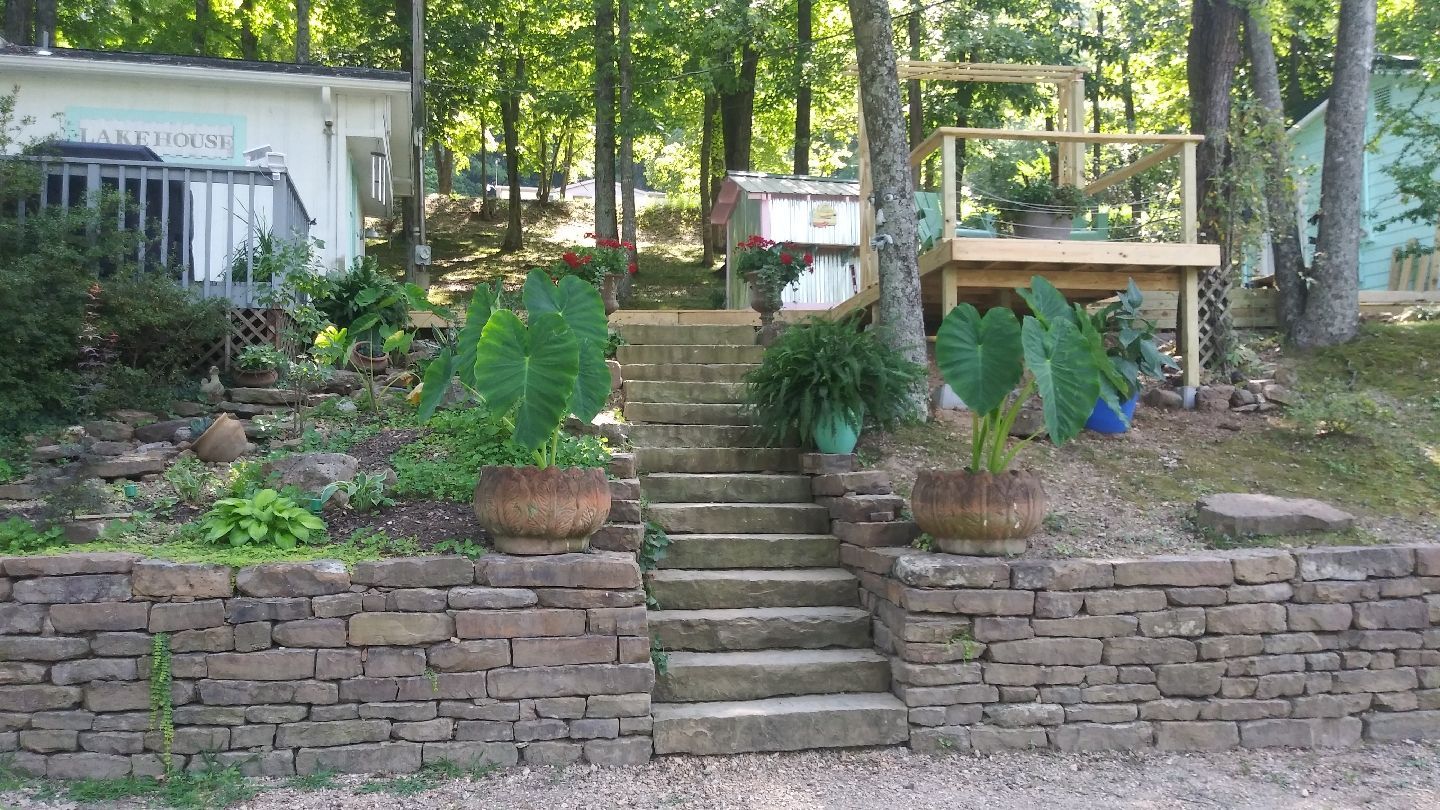 Stone steps lead up a hillside garden with potted plants and a wooden deck.
