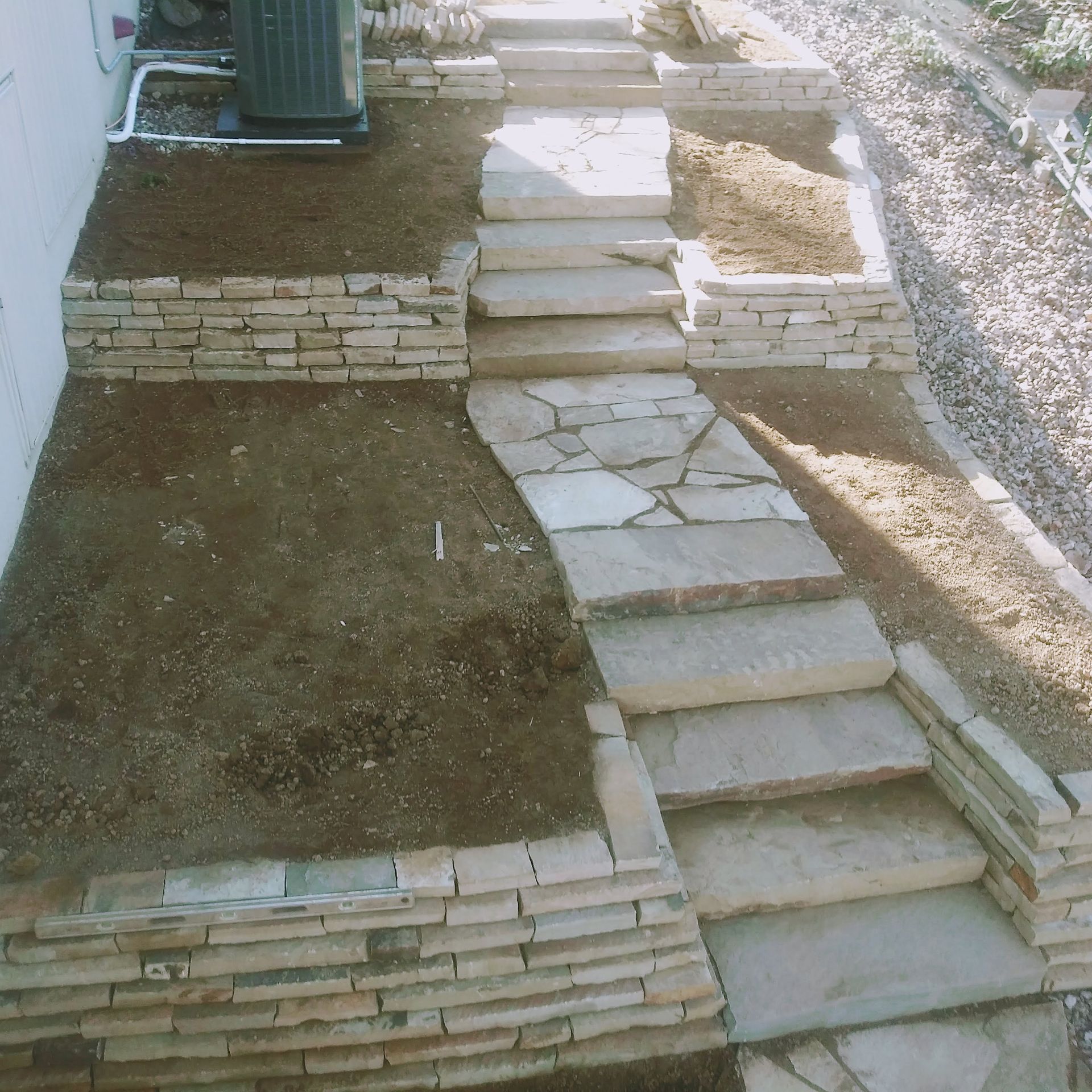 Stone steps and walkway leading uphill through tiered retaining walls, edged with mulch.