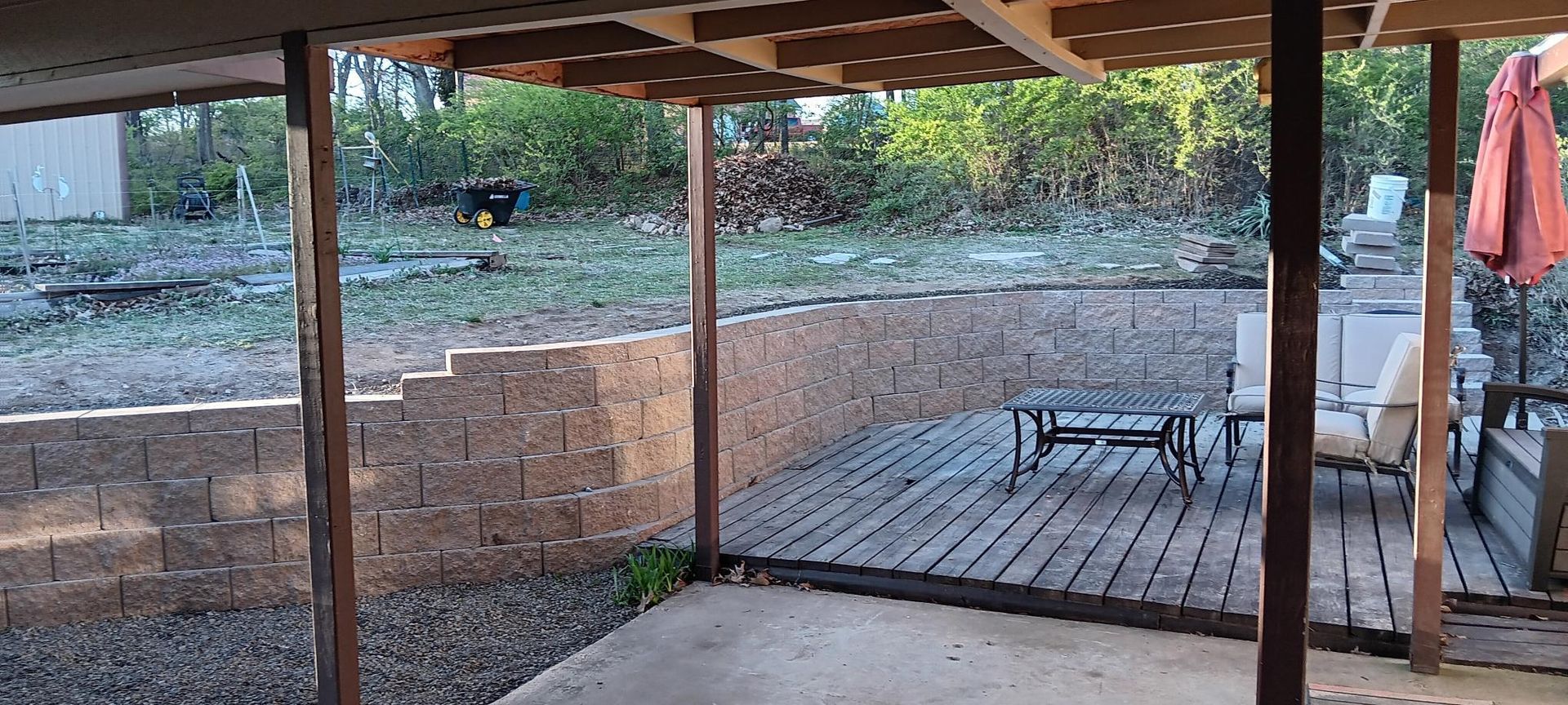 Backyard with a retaining wall, a deck, a table, and a shaded patio area.