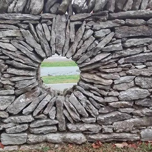 Stone wall with circular opening; green scenery visible through the hole.