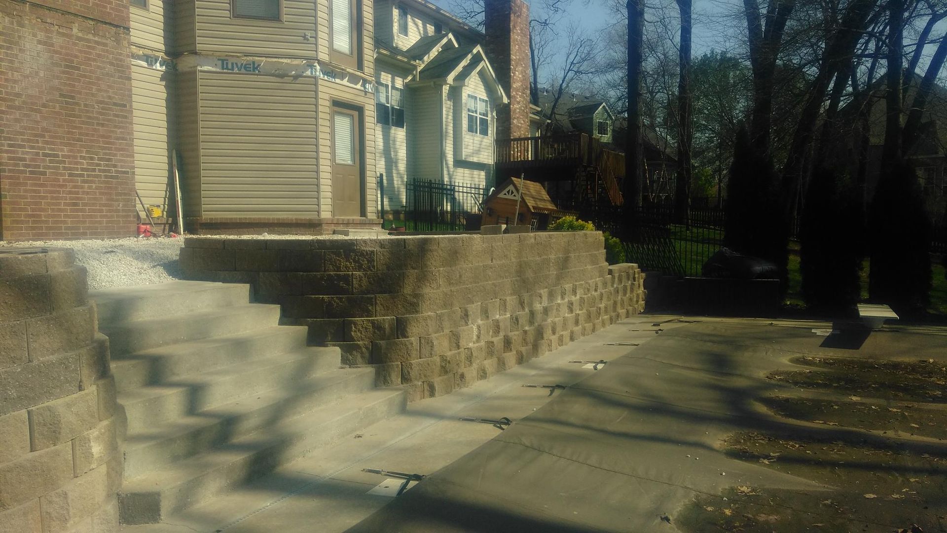 Stone retaining wall with concrete steps leading to a house, sunny day.