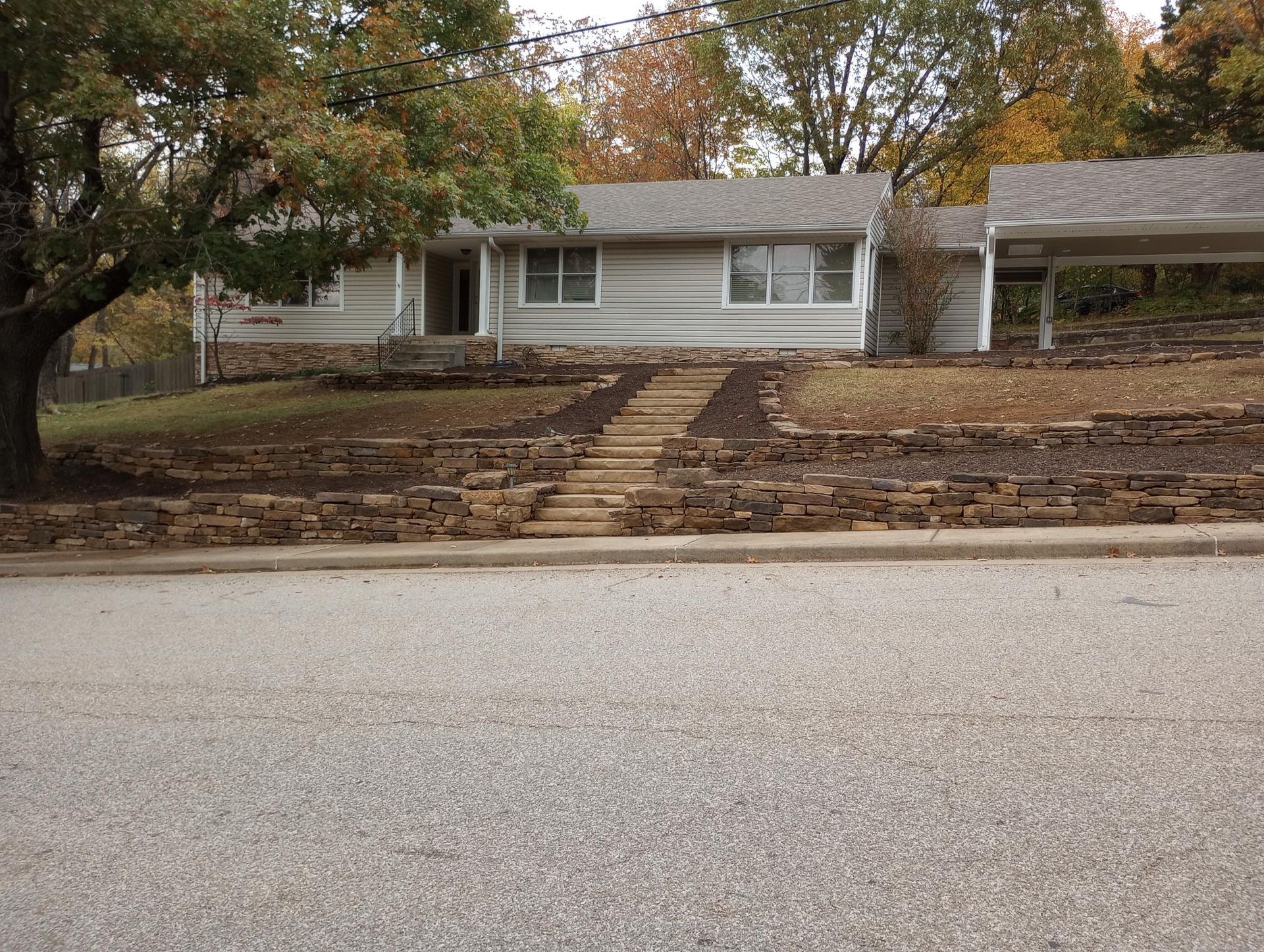 Grey house with stone landscaping and a carport; fall foliage.