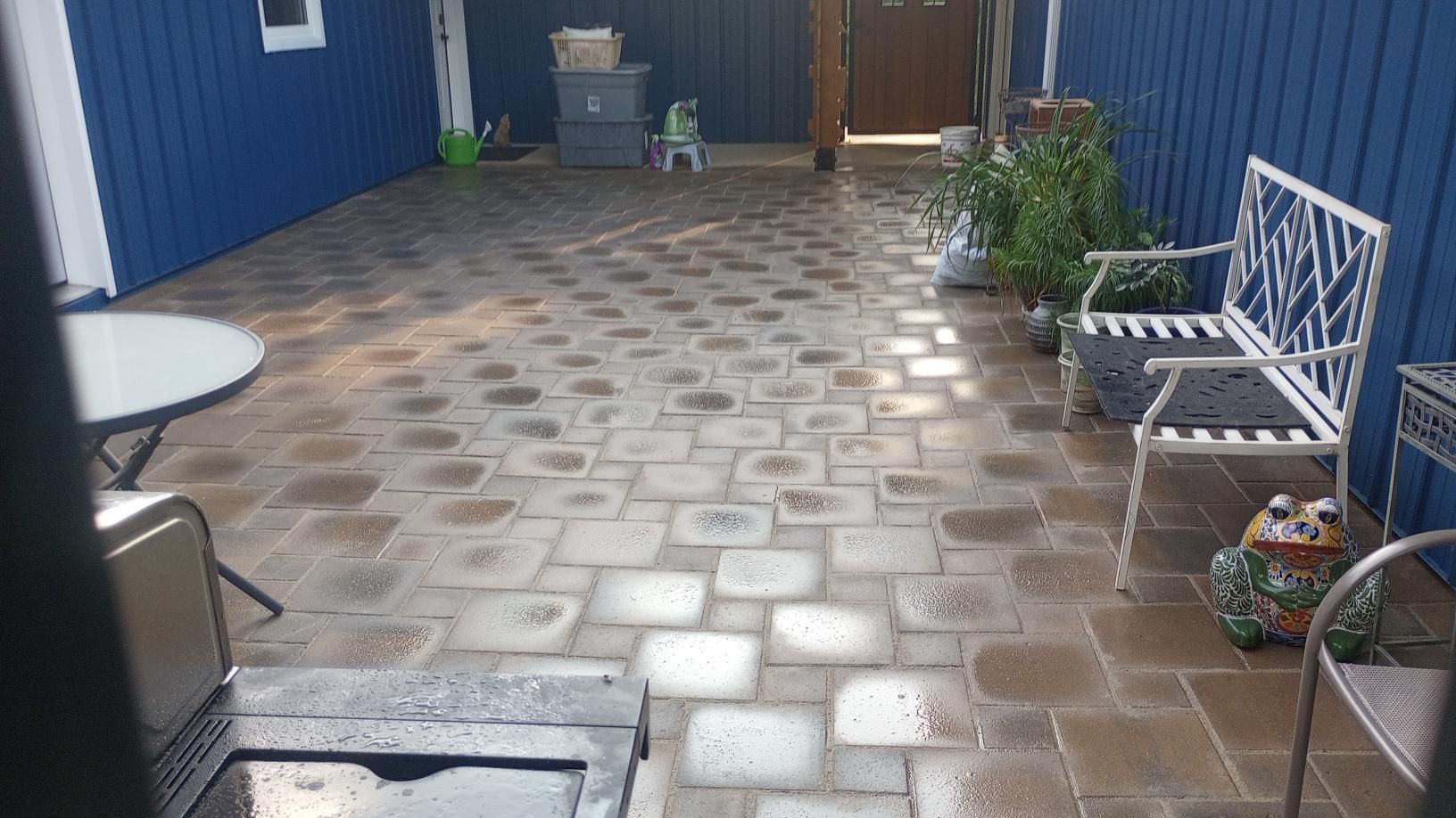 Patio with blue walls, patterned brick floor, white bench, table, and plants.