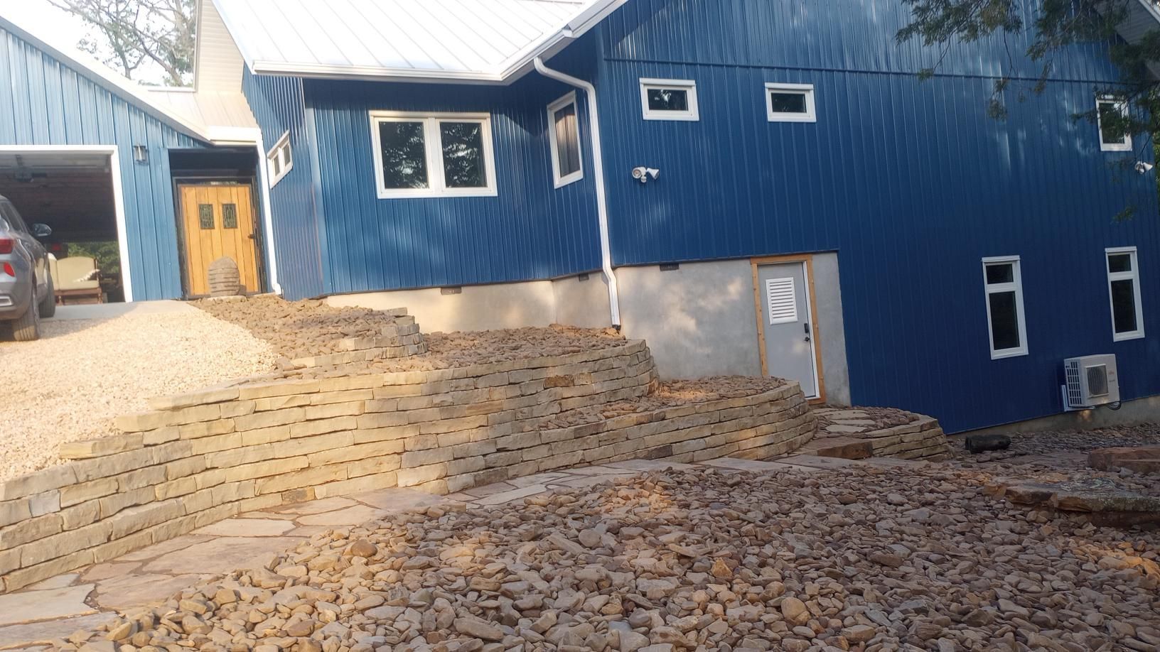 Blue house with gravel landscaping; a car is in a garage on the left.