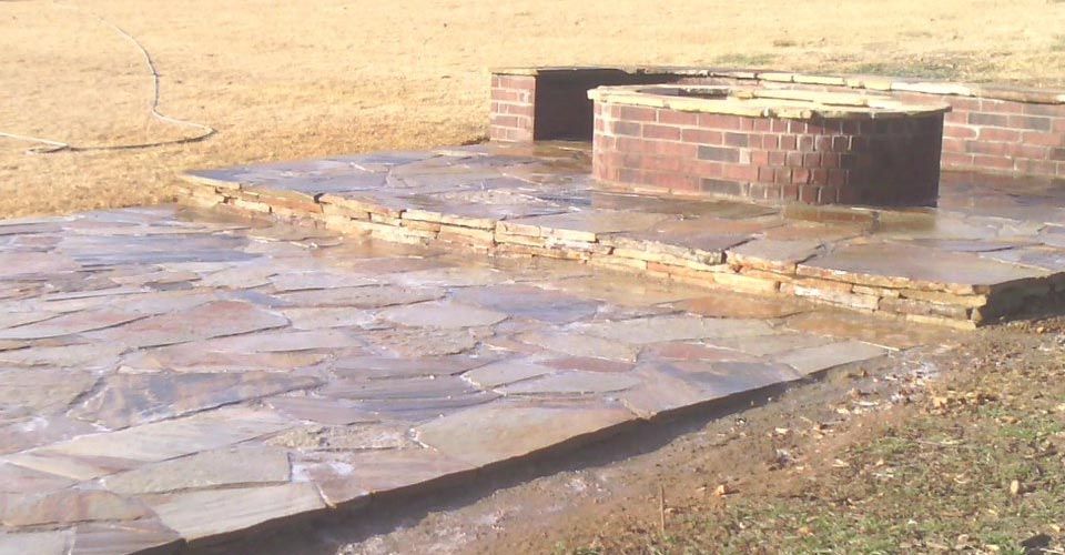 Brick fire pit and stone patio in a grassy outdoor setting.