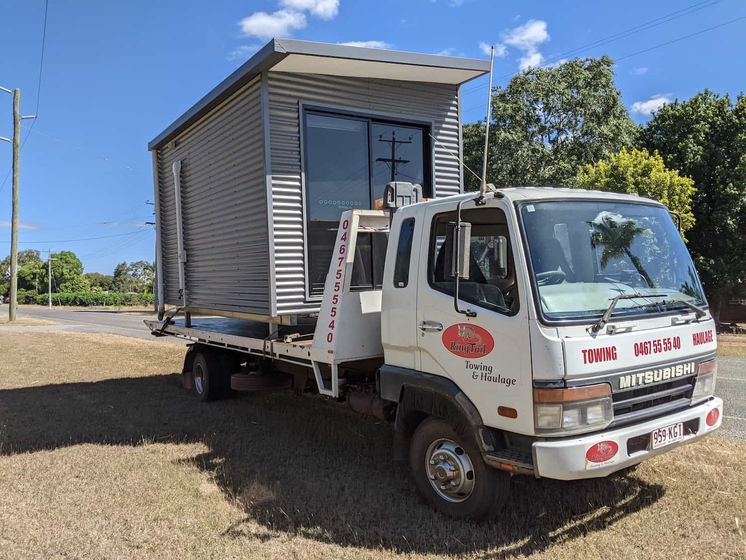 White Truck Carrying a Corrugated Metal Tiny House on a Sunny Day — Ringtail Towing in Mareeba, QLD