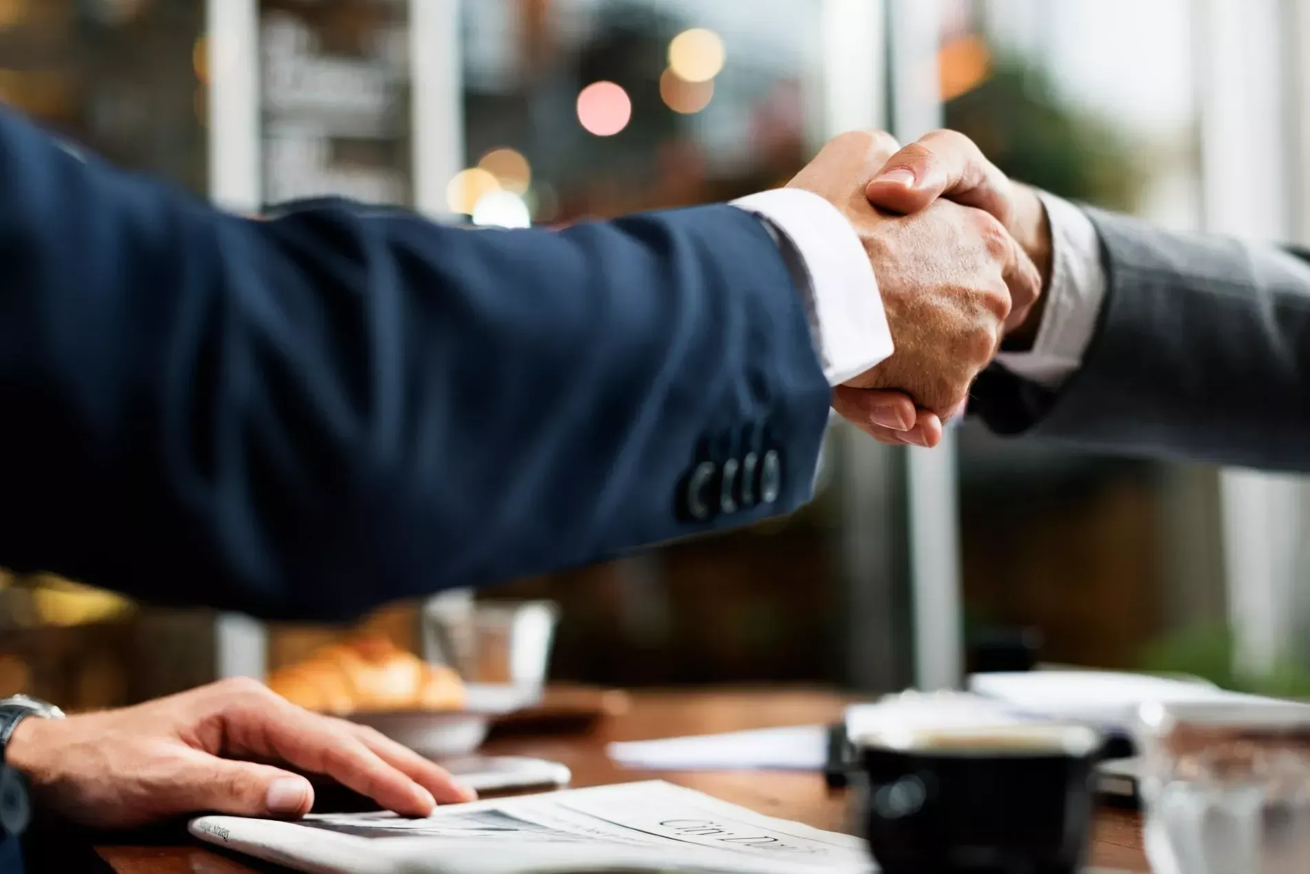 Two men in suits shaking hands over a table, likely closing a deal.