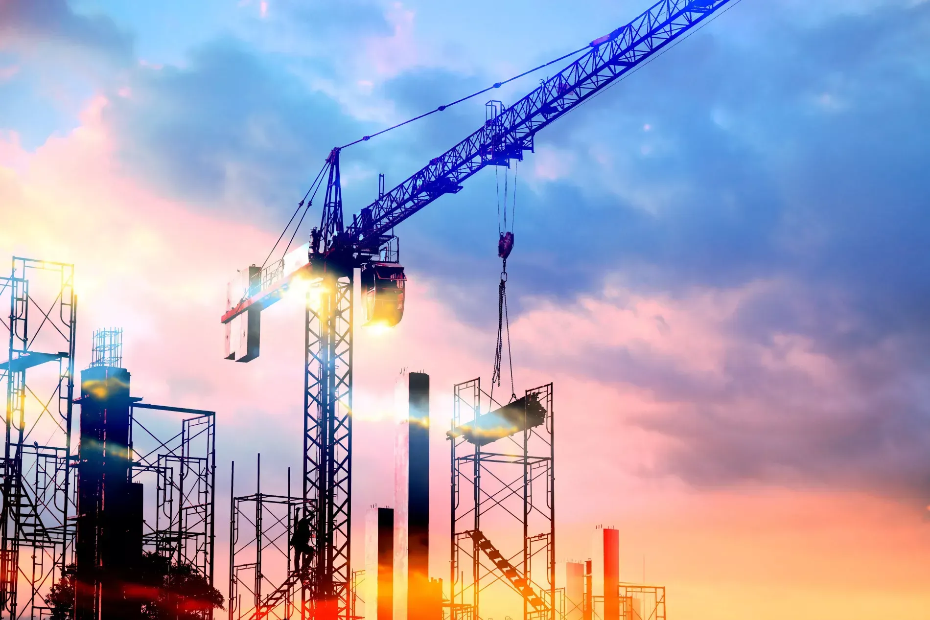 Construction site with crane against a colorful sunset sky, building a new structure.