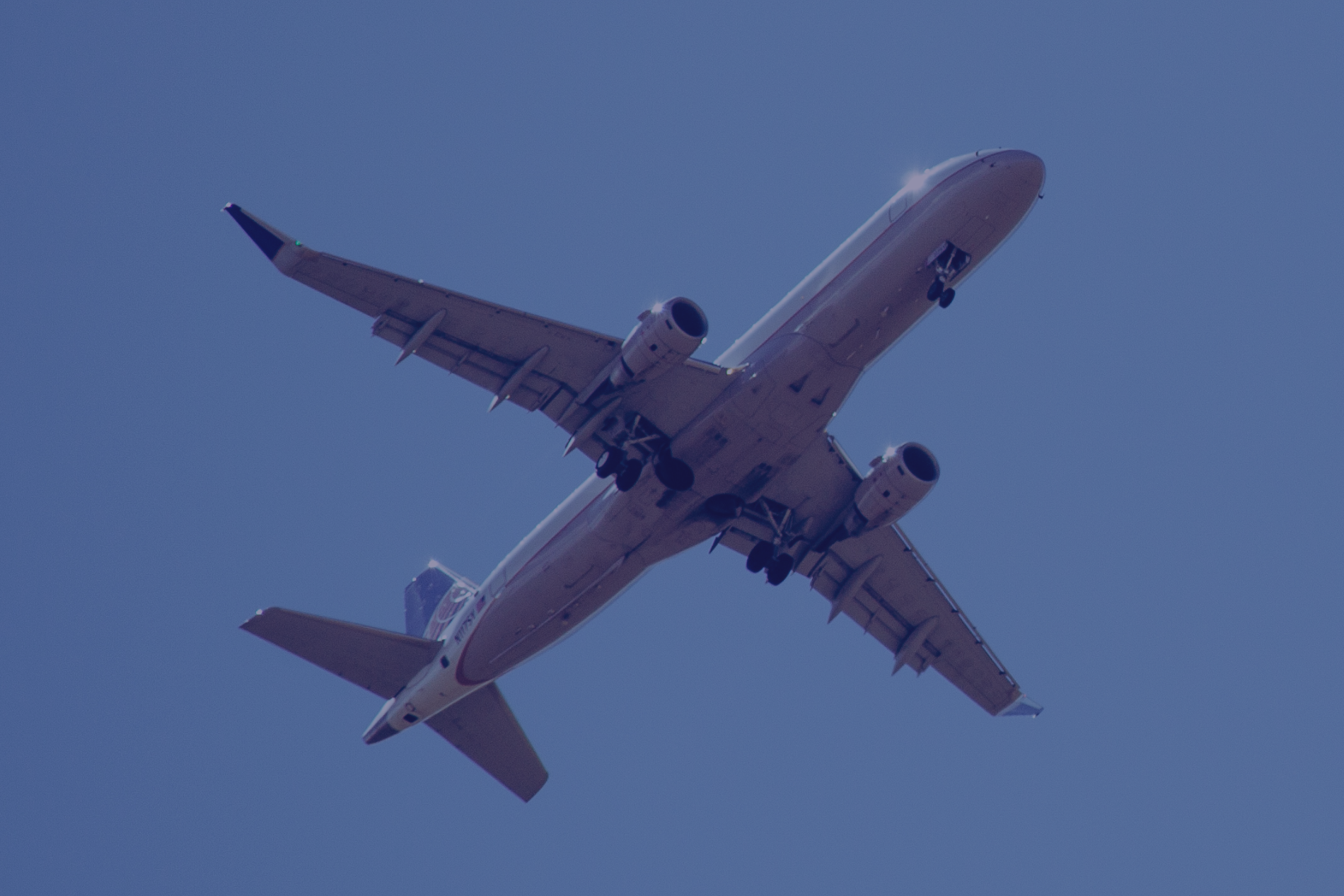 Airplane soaring in a clear, blue sky; landing gear visible.