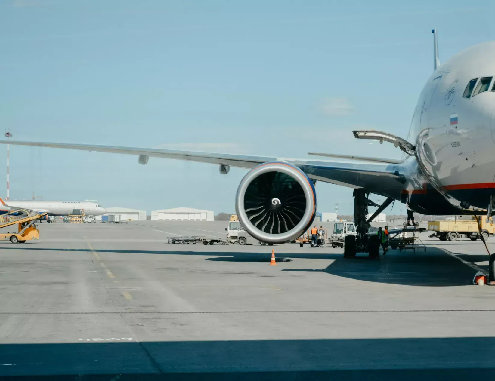 Airplane on tarmac with wing, engine, and airport background.