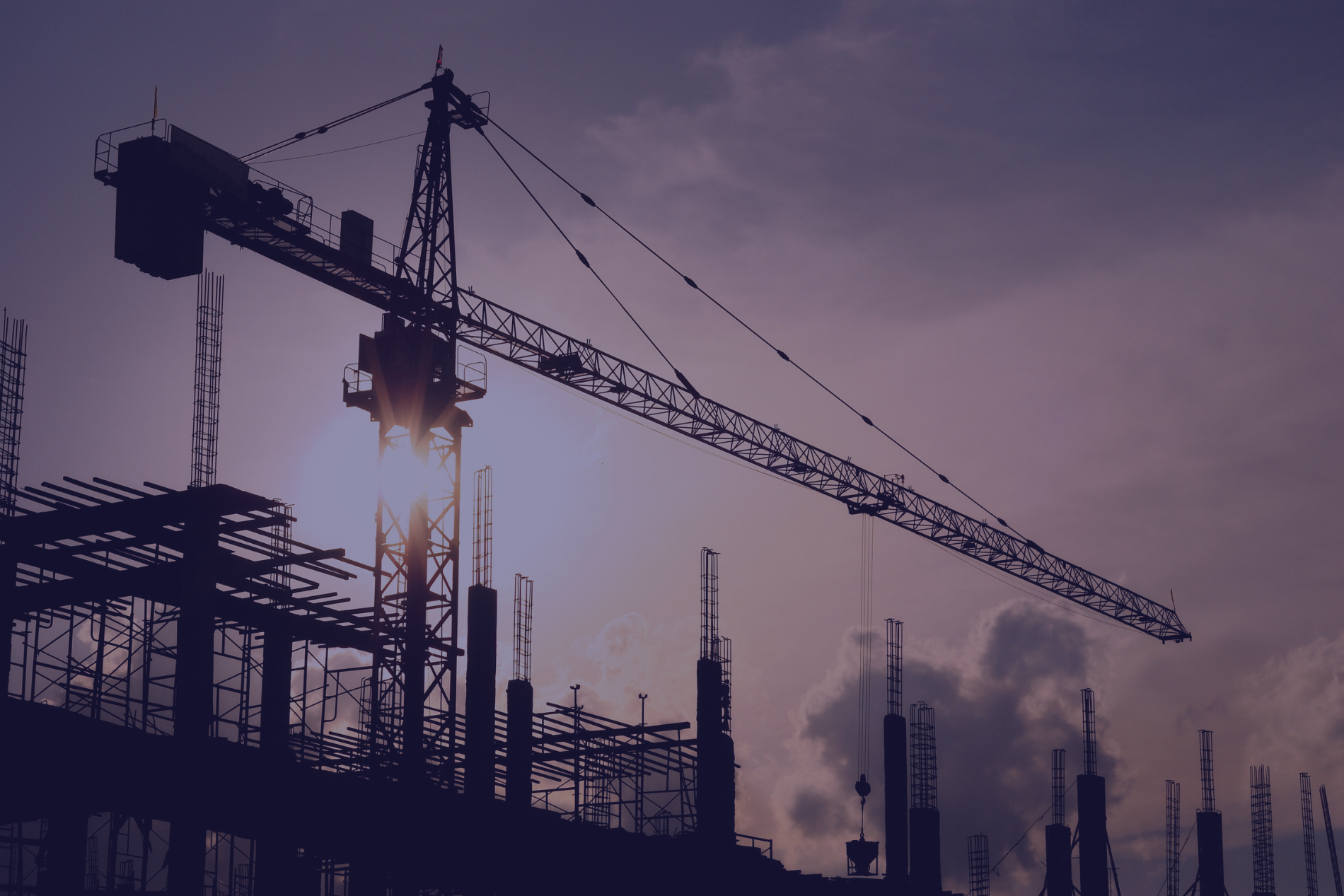 Construction site silhouette with crane against a sunset sky.