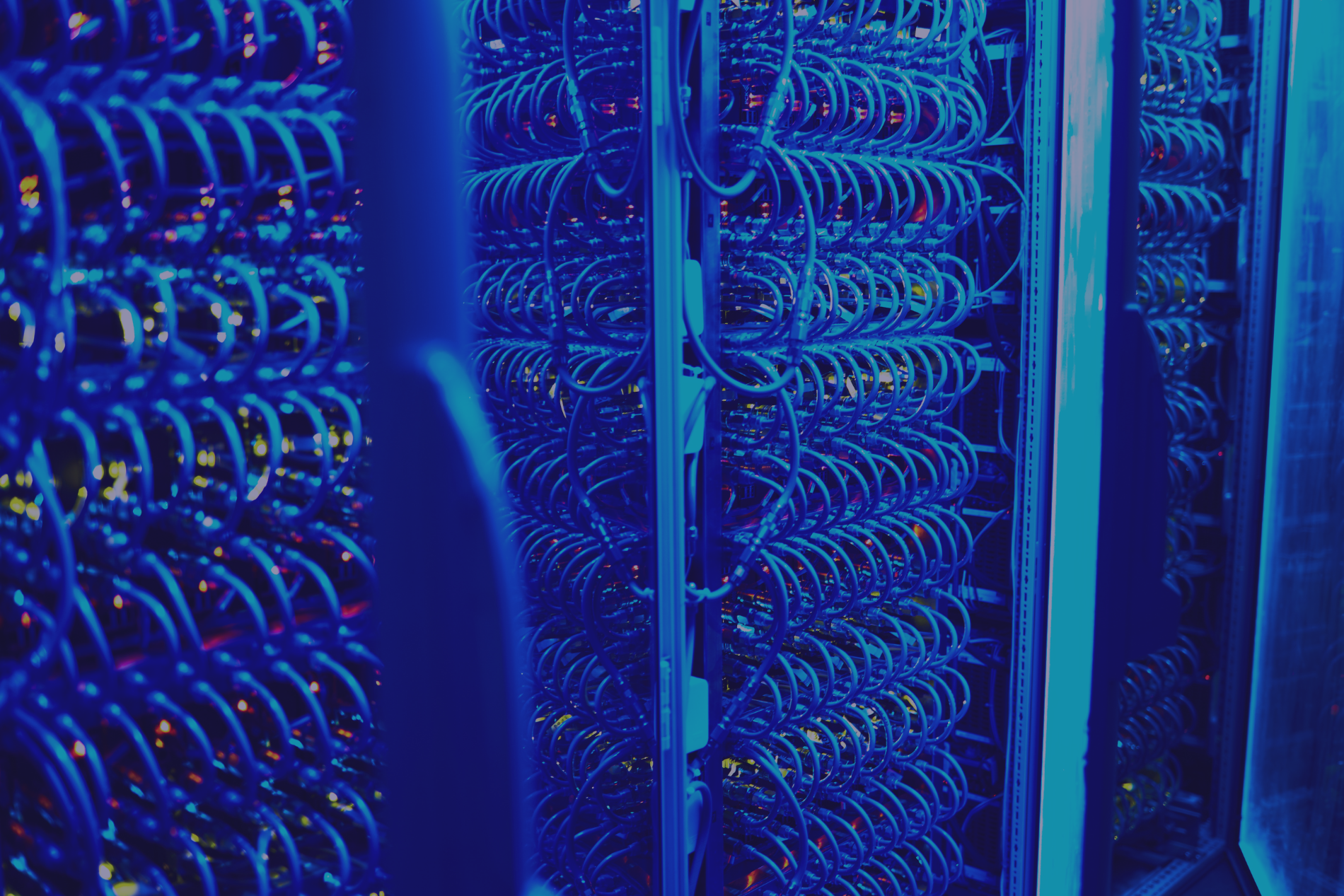 Rows of server racks with a dense network of blue cables in a dark room.