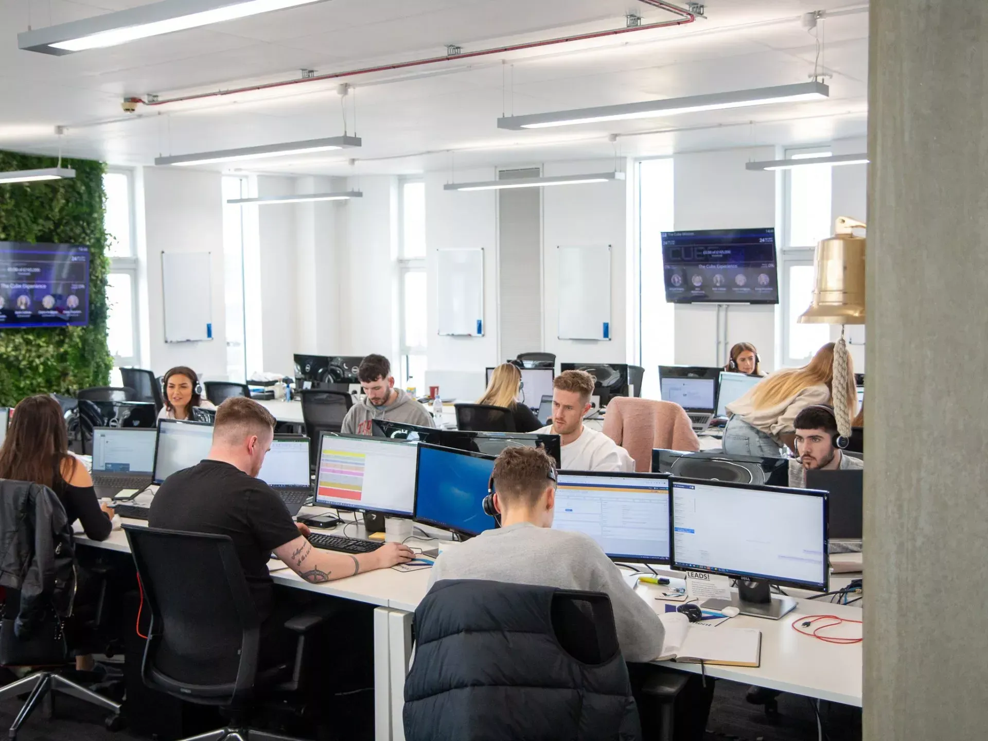 Office with several people working at desks with computers, some looking at screens.