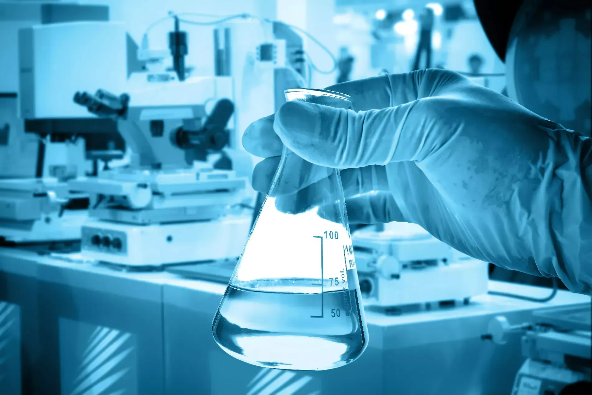 Gloved hand holding a flask with liquid inside a laboratory.