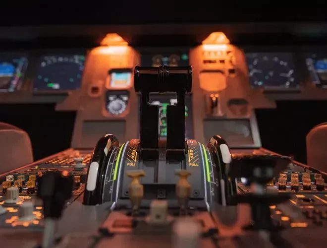 Cockpit view of aircraft controls, lit by warm lights. Focus on throttle levers with illuminated indicators.