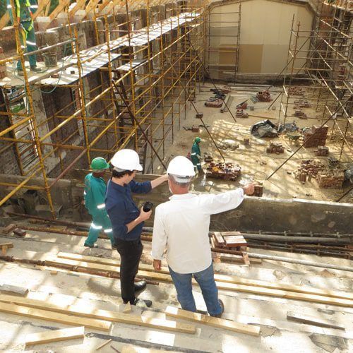 Construction site: workers with hard hats inspect interior of a building, surrounded by scaffolding and debris.