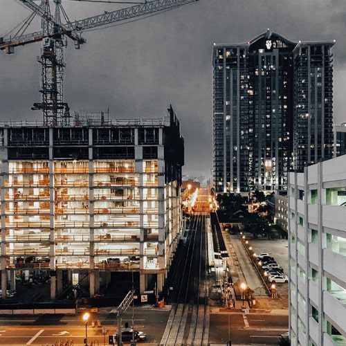 Construction site with tall buildings, a crane, and nighttime city lights.