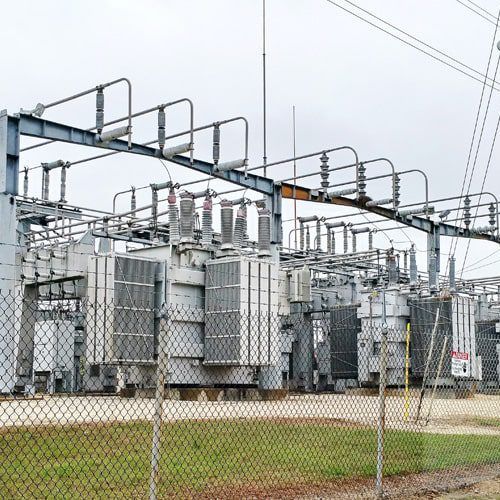Electrical power substation with transformers, fenced in, overcast sky.