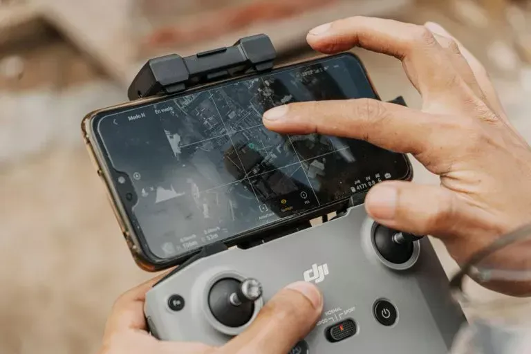 Person holding a drone remote control with a smartphone attached, screen showing a map, finger touching the screen.