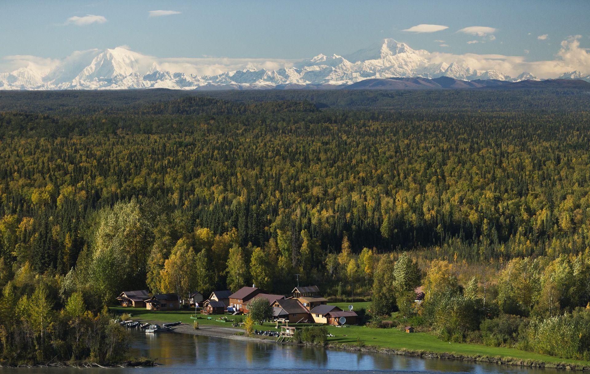 Lodge nestled on a riverbank with fall foliage, and mountains