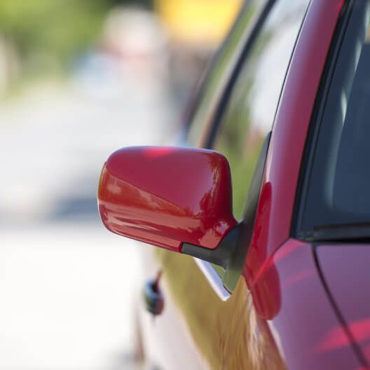 A close up of a red car 's side mirror