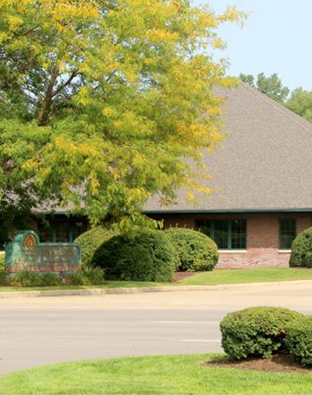 A large brick building with a sign in front of it is surrounded by trees and bushes.