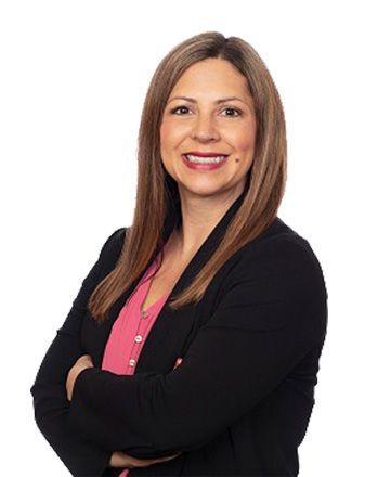 A woman in a black jacket and pink shirt is standing with her arms crossed.