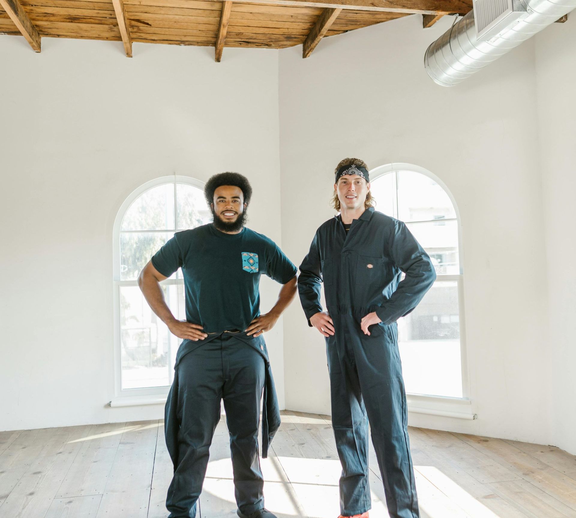 Two men are standing in an empty room with their hands on their hips.