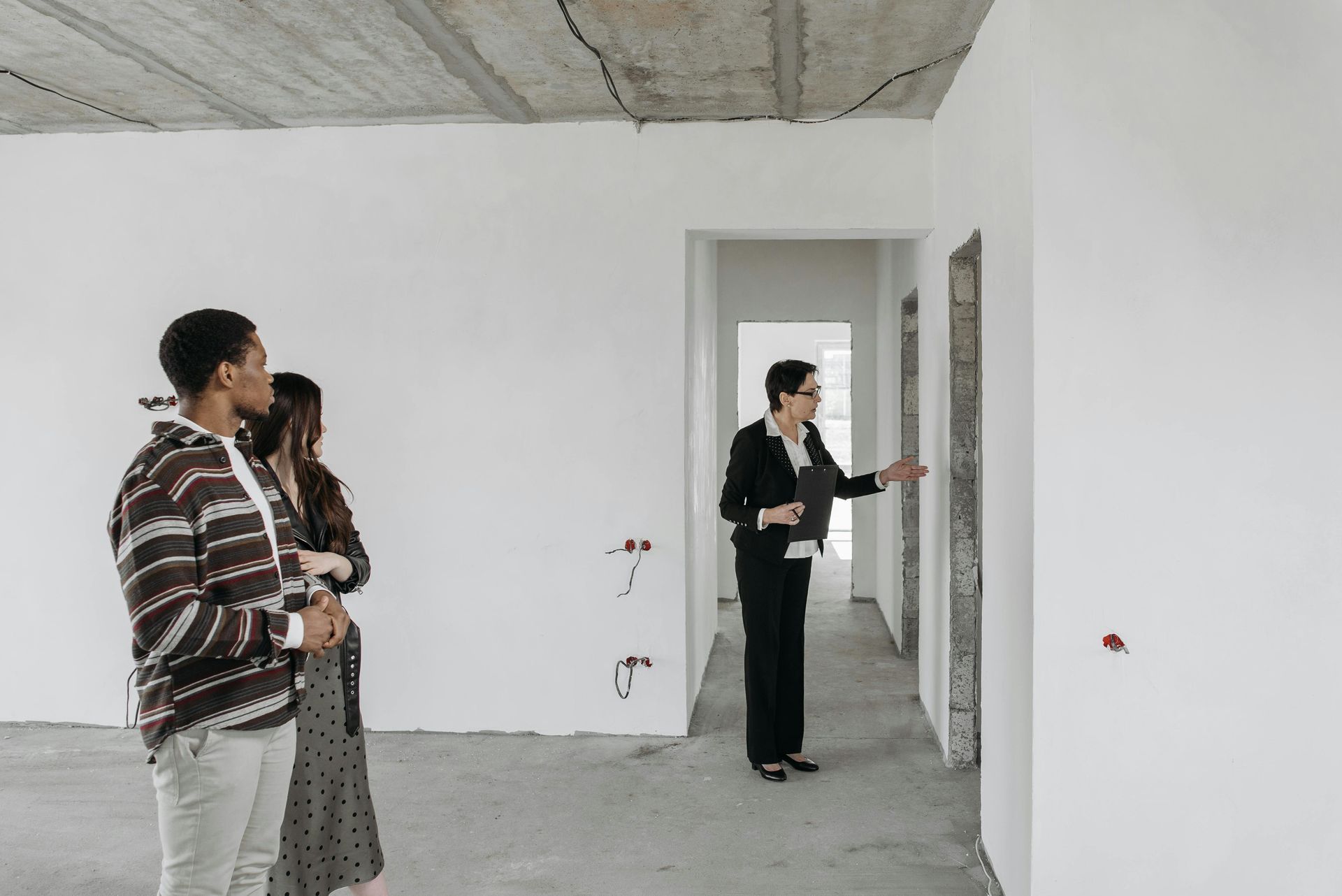 A man and a woman are standing in an empty room looking at a wall.