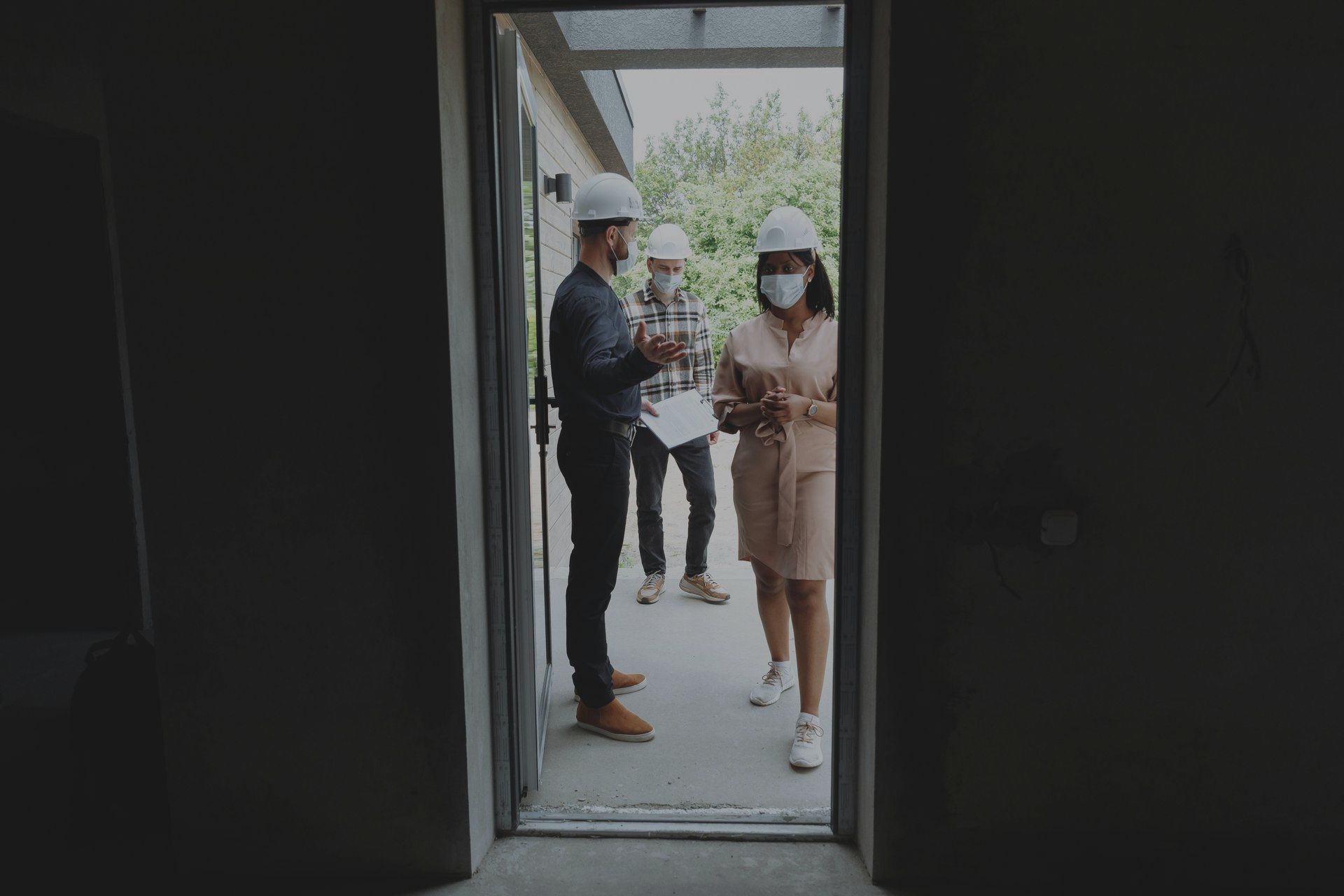A group of people wearing hard hats and masks are standing in front of a door.