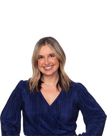 A woman in a blue shirt is smiling and standing with her hands on her hips.