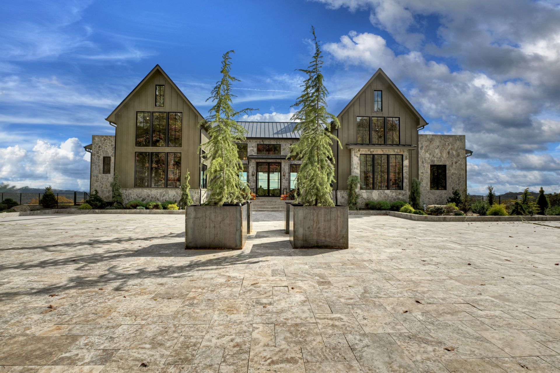 Modern farmhouse with stone and wood exterior, under blue sky, front view, concrete patio.
