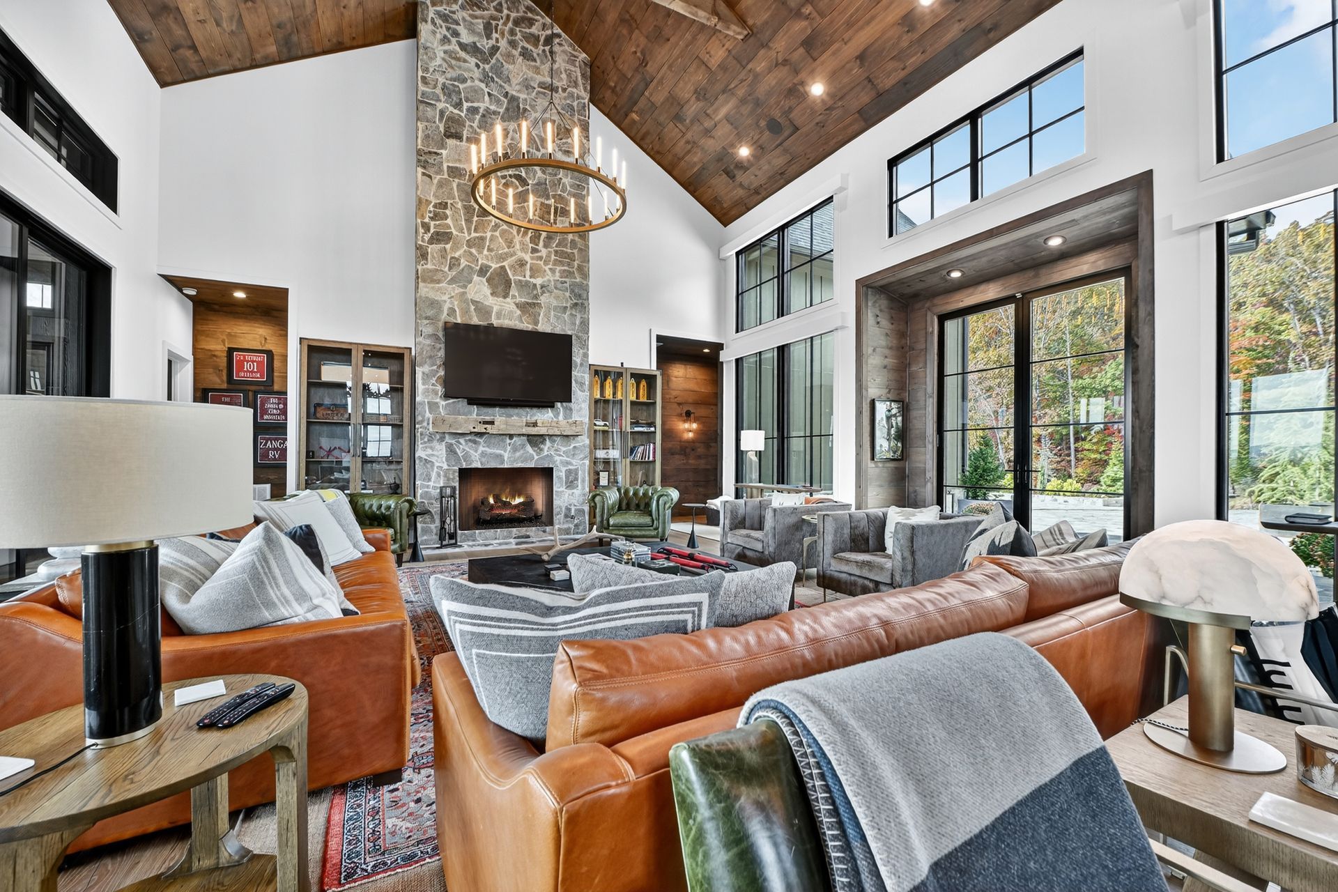 Spacious living room with stone fireplace, brown leather sofas, large windows, and wooden ceiling.
