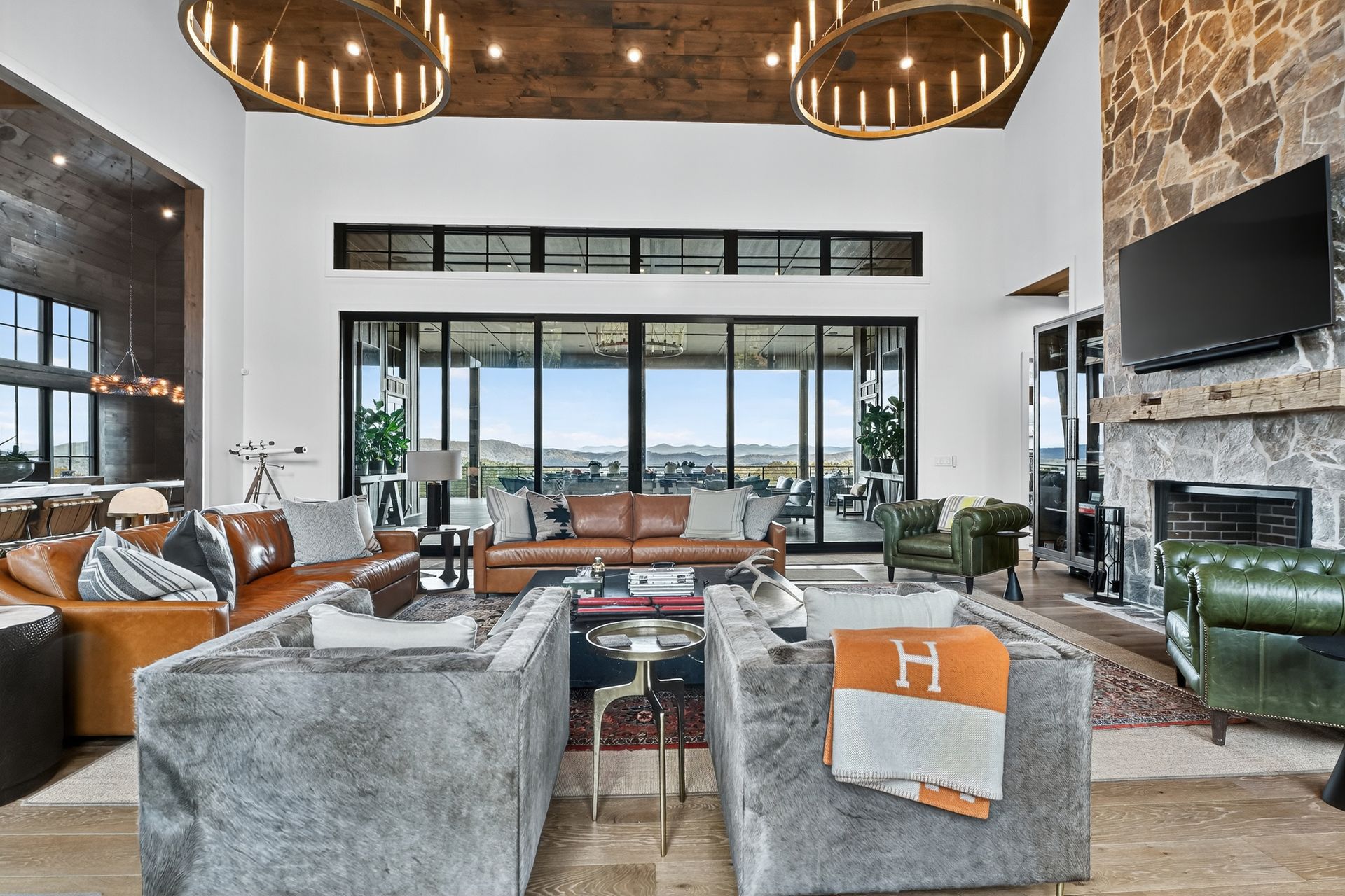 Spacious living room with leather furniture, stone fireplace, and large windows with outdoor views.