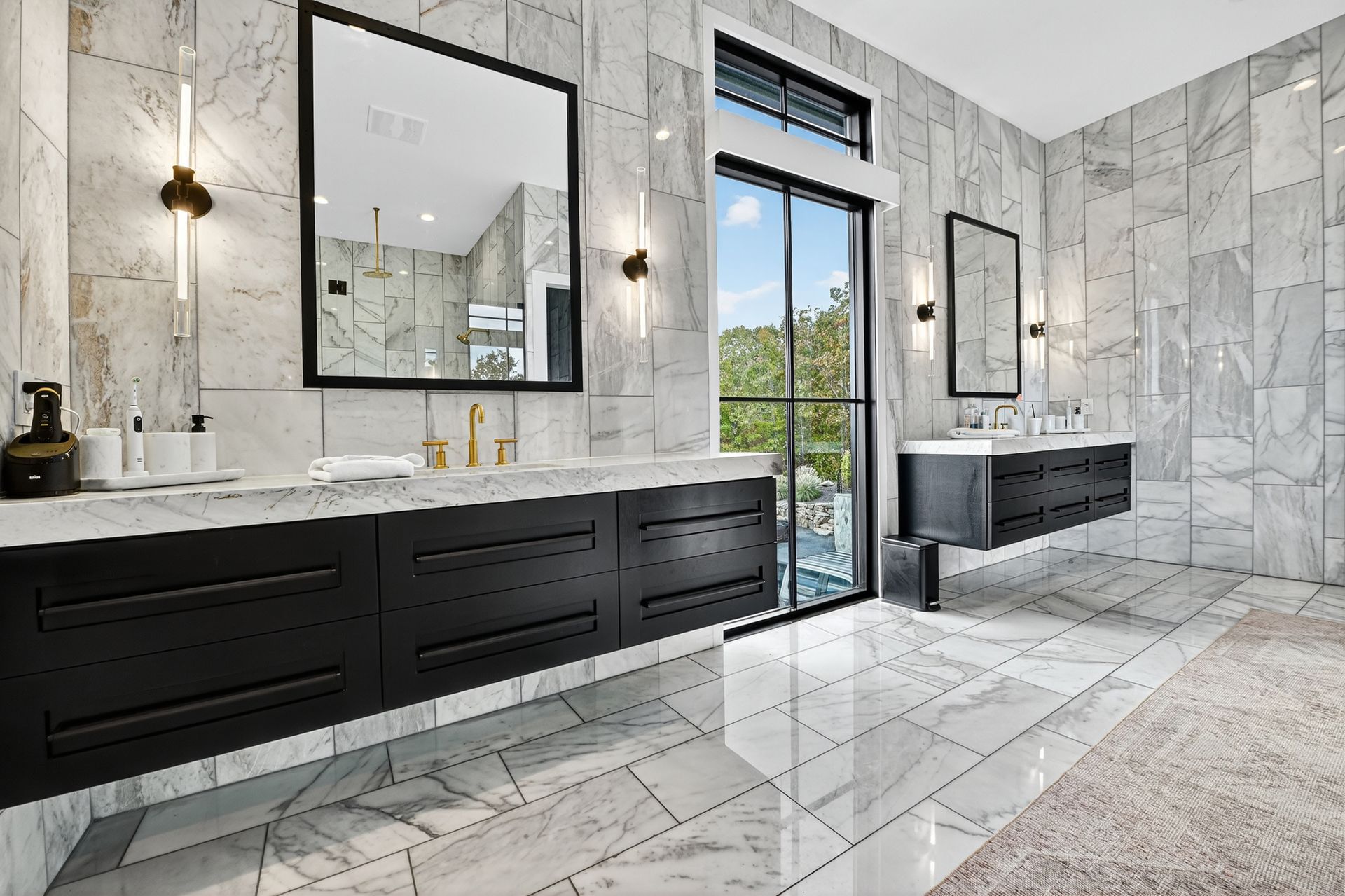 Luxurious bathroom with marble walls and floors, black cabinetry, and a large window.