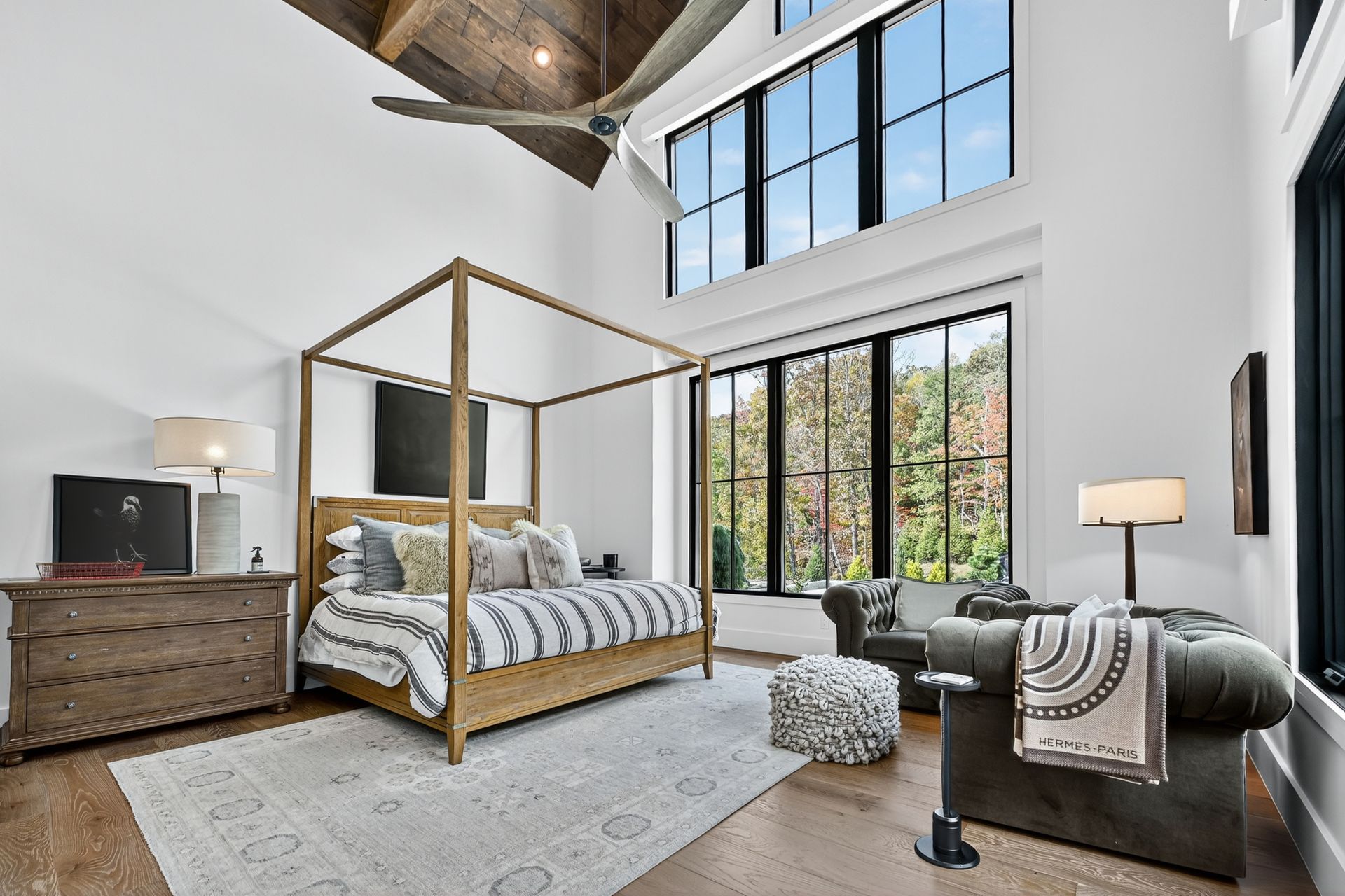 Bedroom with canopy bed, large windows, wood beams, and a seating area.