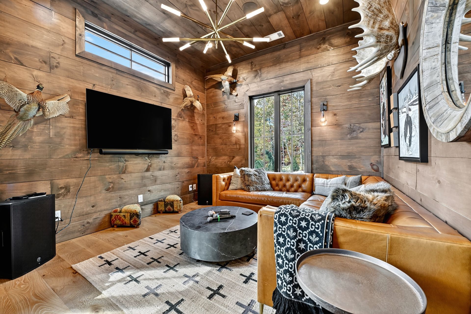 Living room with wood-paneled walls, leather sectional, large TV, and deer antler decor.