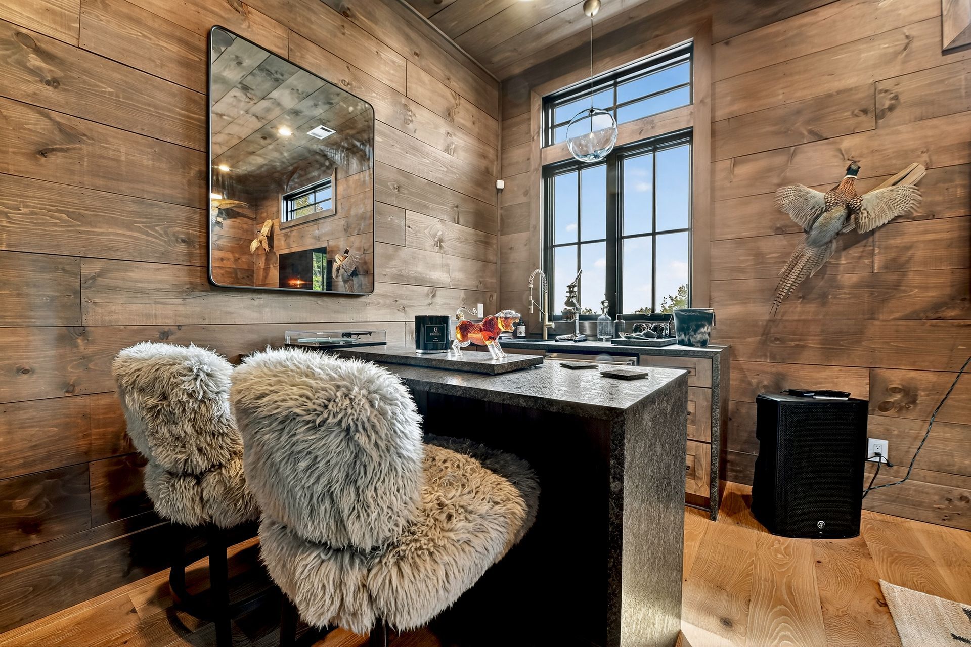 Home bar with wood-paneled walls, a granite counter, two furry stools, and a large window.