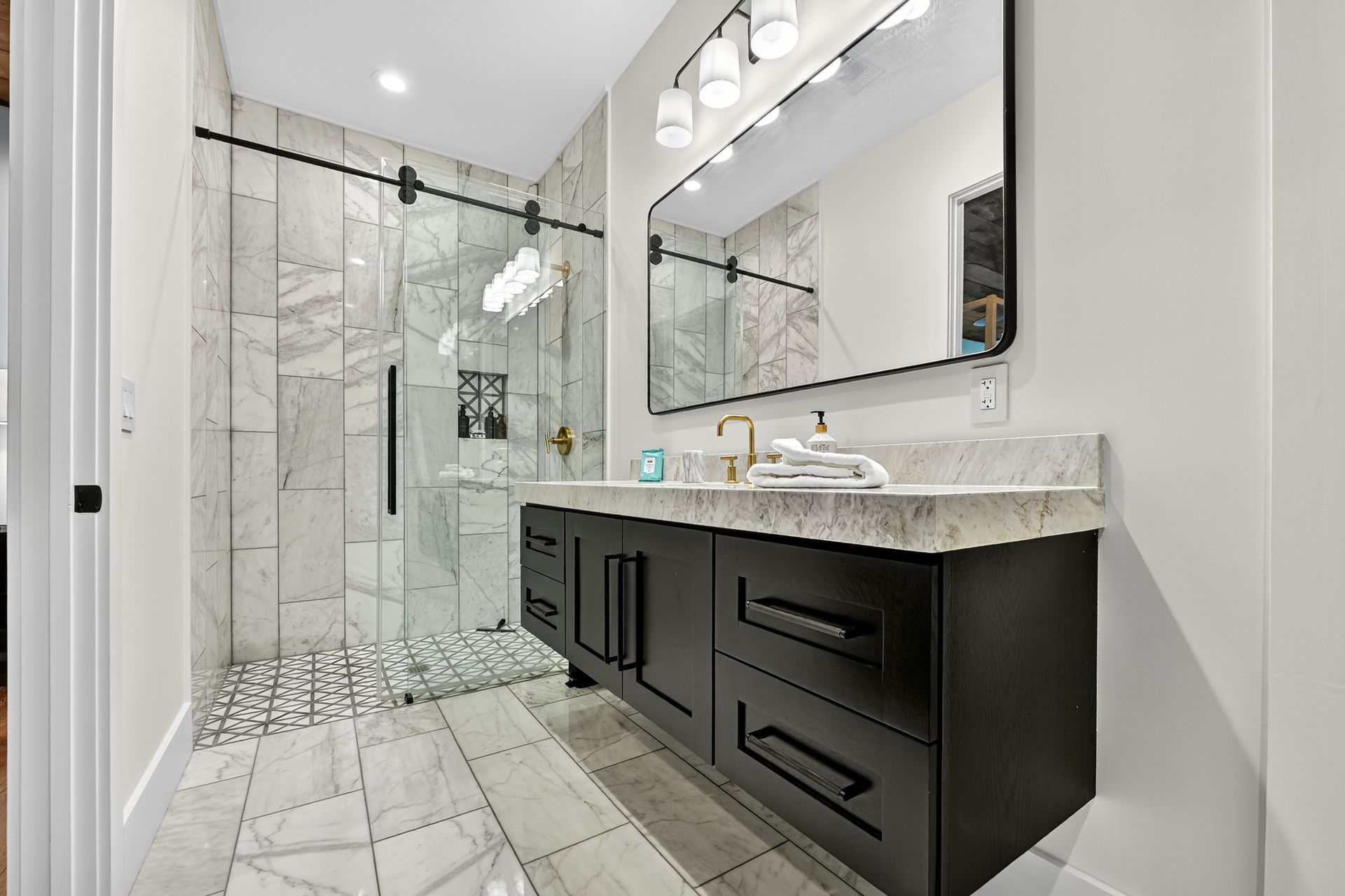 Modern bathroom with marble shower, black vanity, and large mirror.