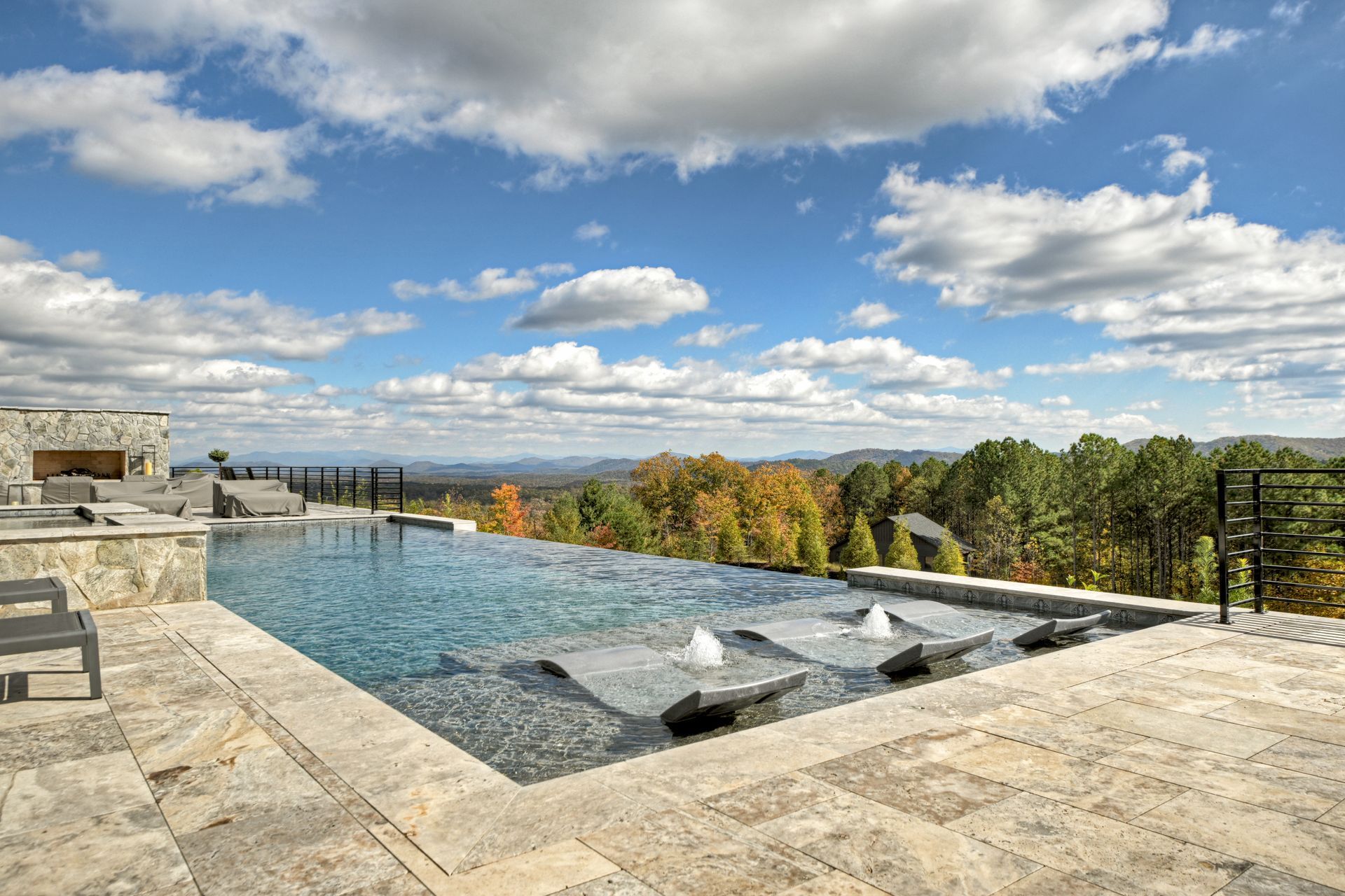 Infinity pool overlooking autumn trees and mountains under a blue sky with clouds.