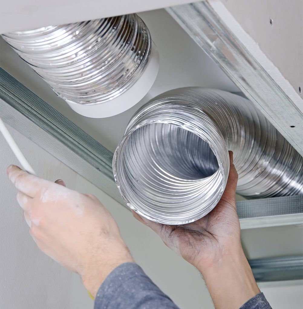 A man is sitting on the ground working on an air conditioner.