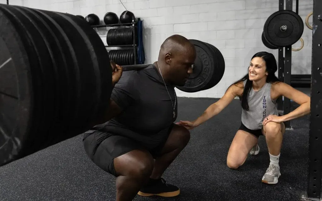 A trainer watches as a person performs a barbell squat in a gym in Moorestown, NJ.