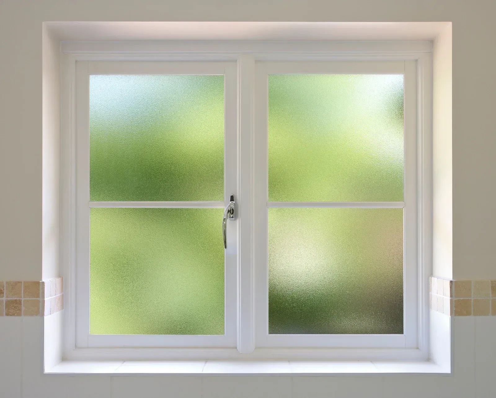 White-framed window with textured glass, overlooking a blurry green outdoor scene.