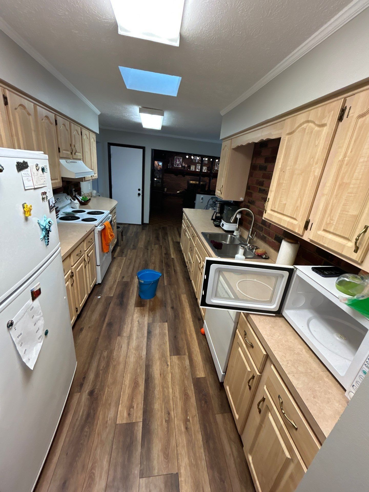 Kitchen with light wood cabinets, appliances, and a blue bucket on the floor