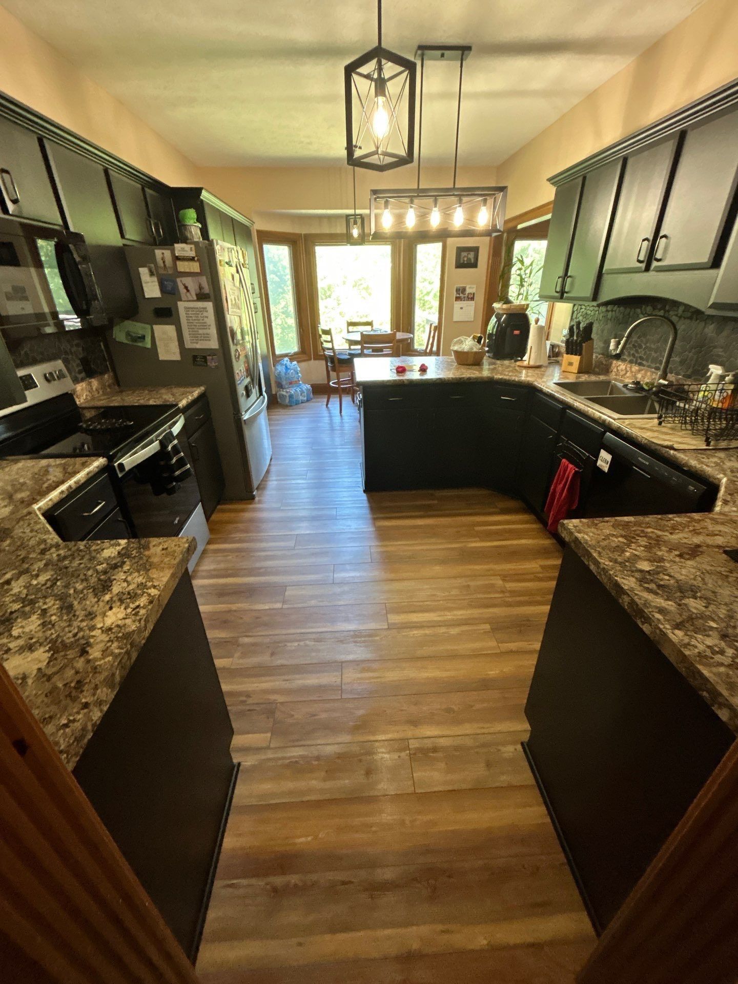 Kitchen with dark cabinets, wood floor, and a view of a dining area through a window
