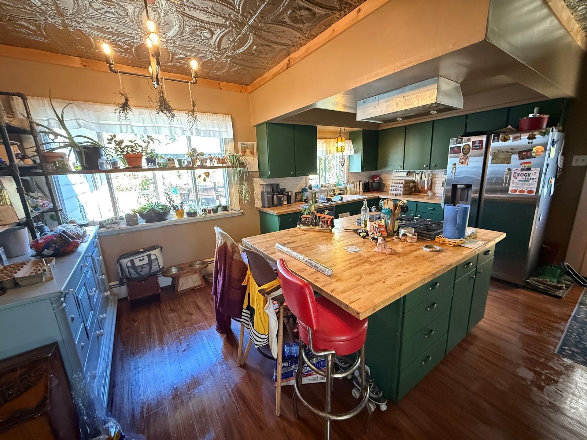 Green kitchen with island, red bar stools, wooden countertops, and a decorative tin ceiling