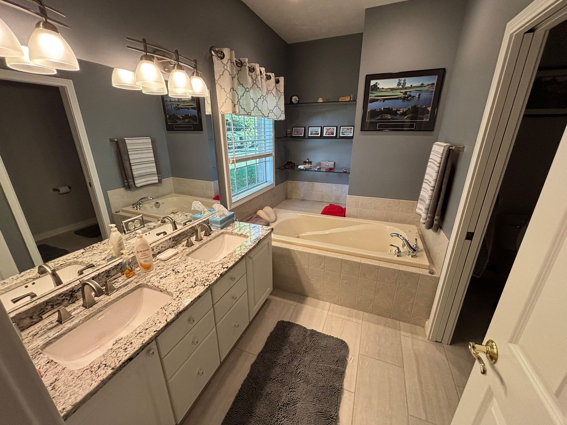 Bathroom with double sinks, tub, gray walls, white cabinets, and artwork