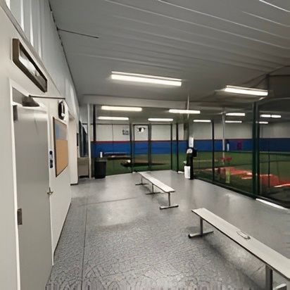 Indoor baseball training facility with batting cages, benches, and a turf field