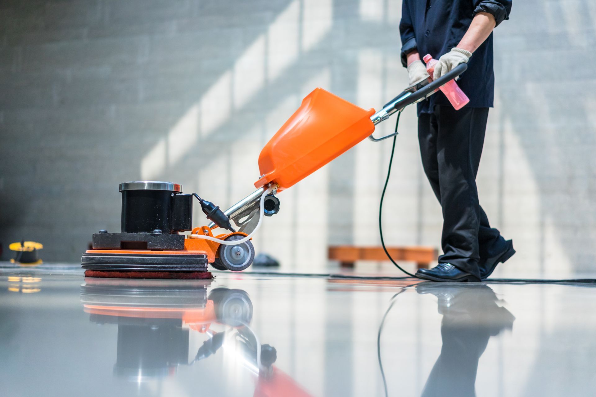 Industrial cleaning service worker polishing warehouse floor with orange buffer machine.