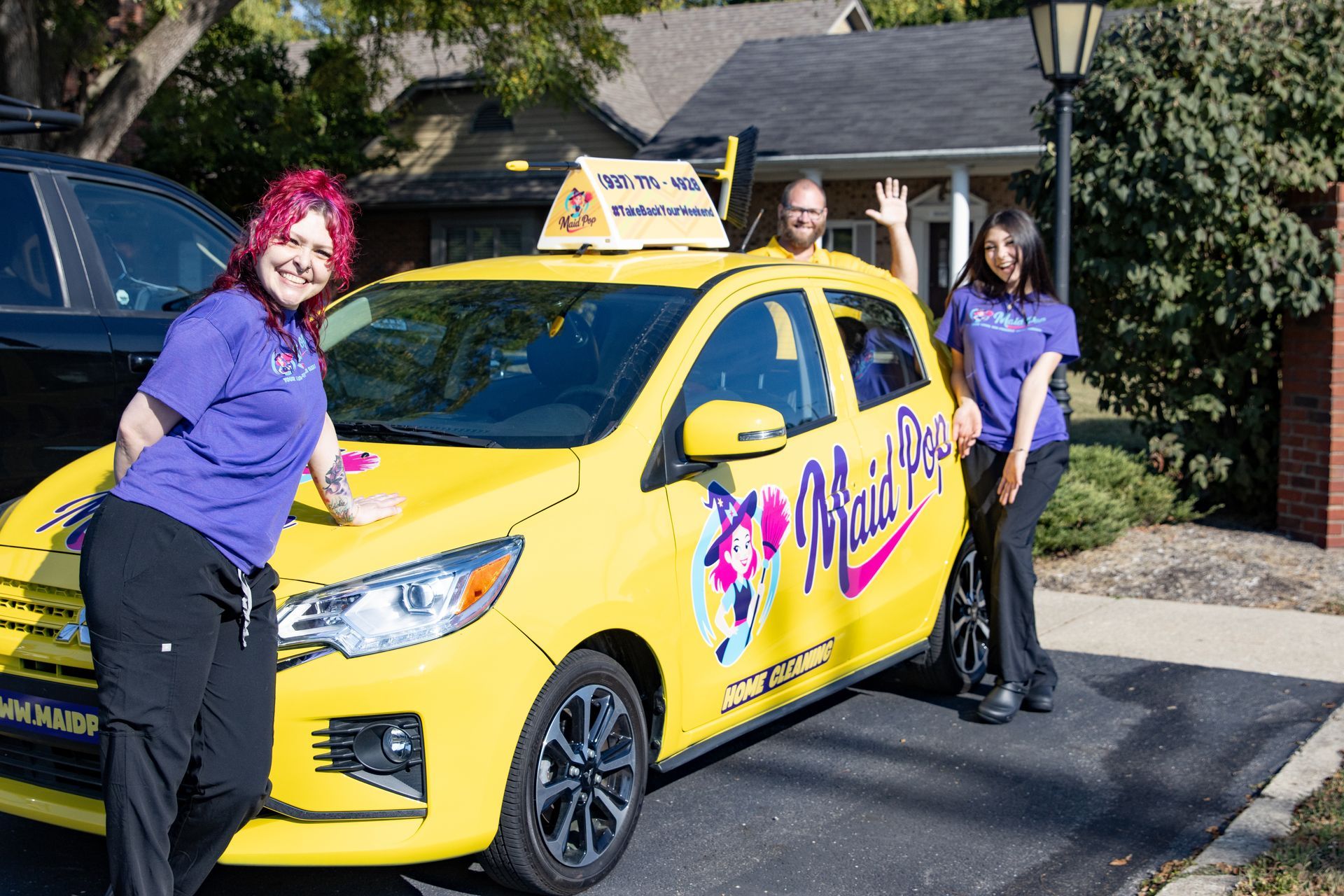 Three people pose with a yellow car